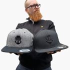a man holding two caps with a logo shamchor