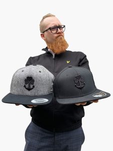 a man holding two caps with a logo shamchor